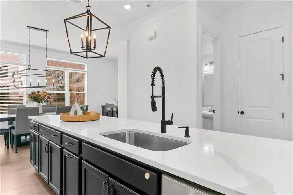 Kitchen featuring ornamental molding, dark cabinetry, light stone countertops, suspended lighting, and light wood-style flooring
