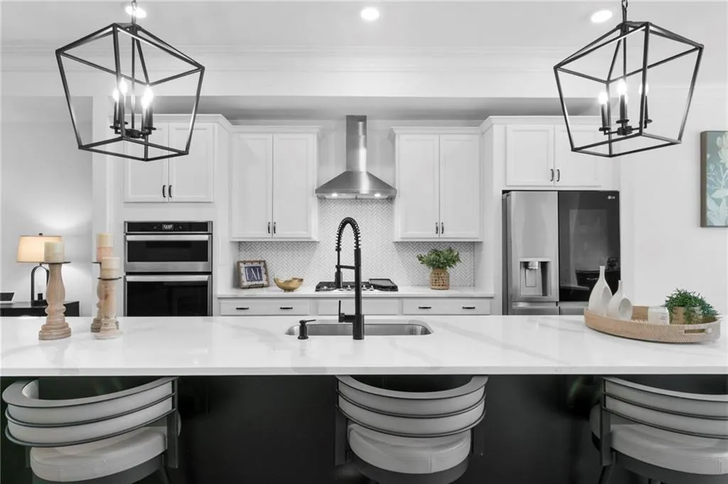 Kitchen featuring suspended lighting, a breakfast bar area, stainless steel appliances, light stone countertops, and two tone cabinetry