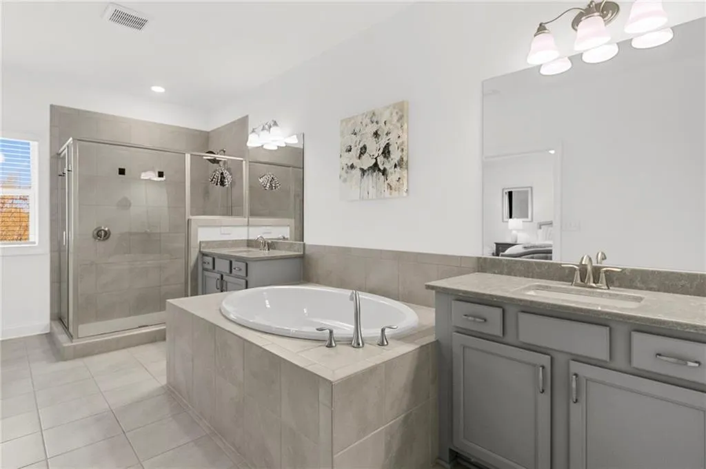 Full bath with two vanities, a garden tub, light tile patterned floors, and a shower stall