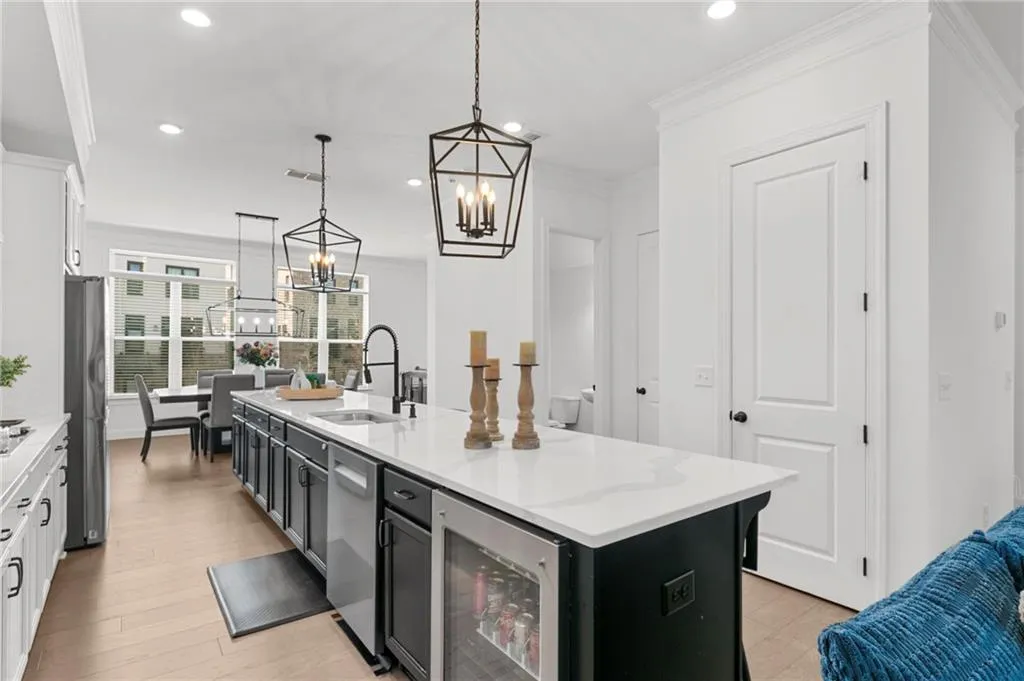 Dual tone kitchen with two tone color scheme, a kitchen island with sink, wine cooler, ornamental molding, and light stone countertops