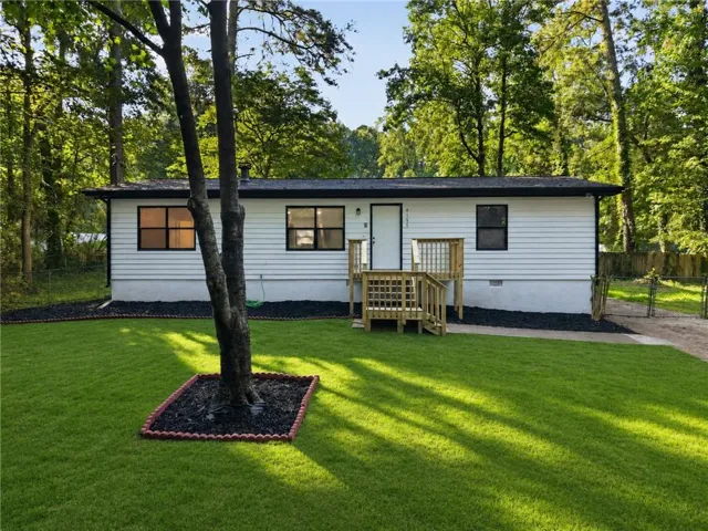White horizontal siding exterior with black window frames, a natural wood deck, and a manicured lawn