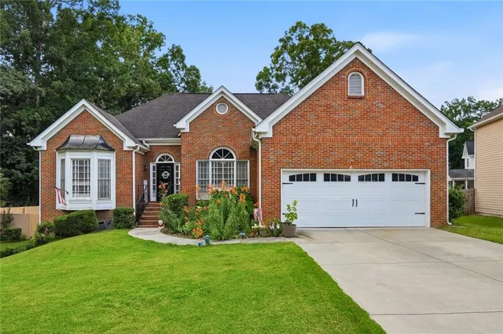 Brick exterior featuring a two-car garage, concrete driveway, and manicured front lawn