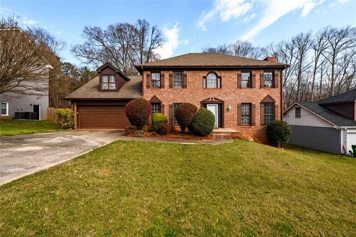 View of front facade featuring a front yard, concrete driveway, brick siding, and a chimney