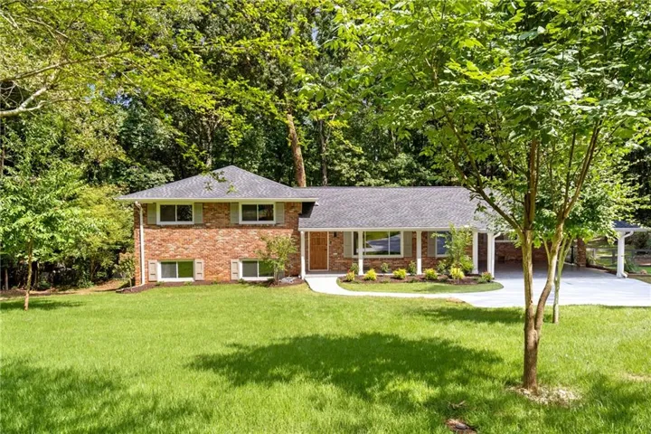 Brick exterior featuring a covered front porch, manicured lawn, paved driveway, and established trees