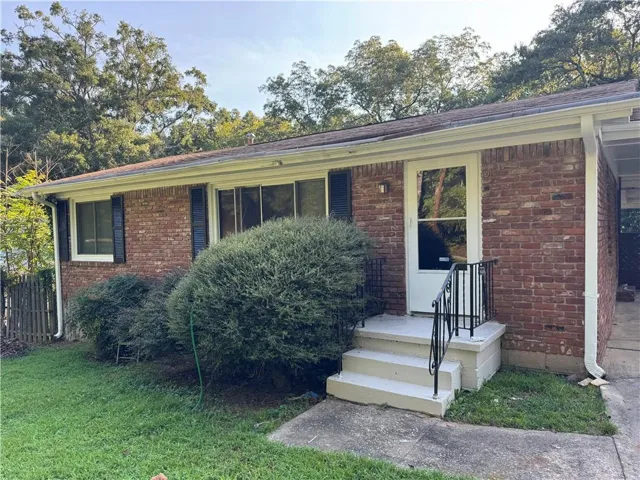 Red brick exterior with white trim, black window shutters, and a white storm door