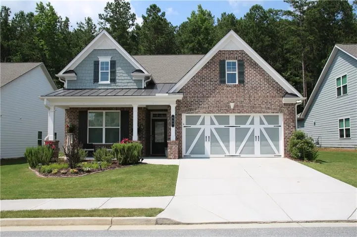 Brick and siding exterior featuring a covered porch with white columns, a metal roof accent, and decorative garage doors
