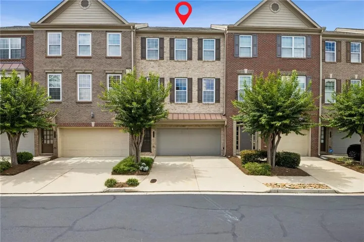 Three-story townhome featuring a brick facade with a gabled accent and a two-car garage