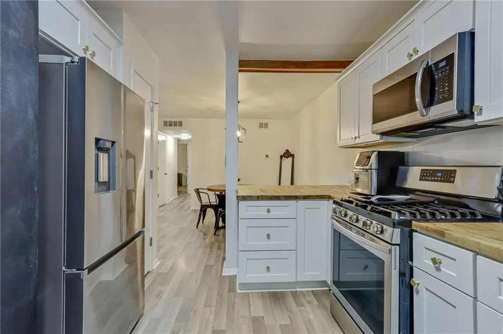 Kitchen with appliances with stainless steel finishes, a peninsula, light wood-style floors, and white cabinetry Kitchen with appliances with stainless steel finishes, a peninsula, light wood-style floors, and white cabinetry