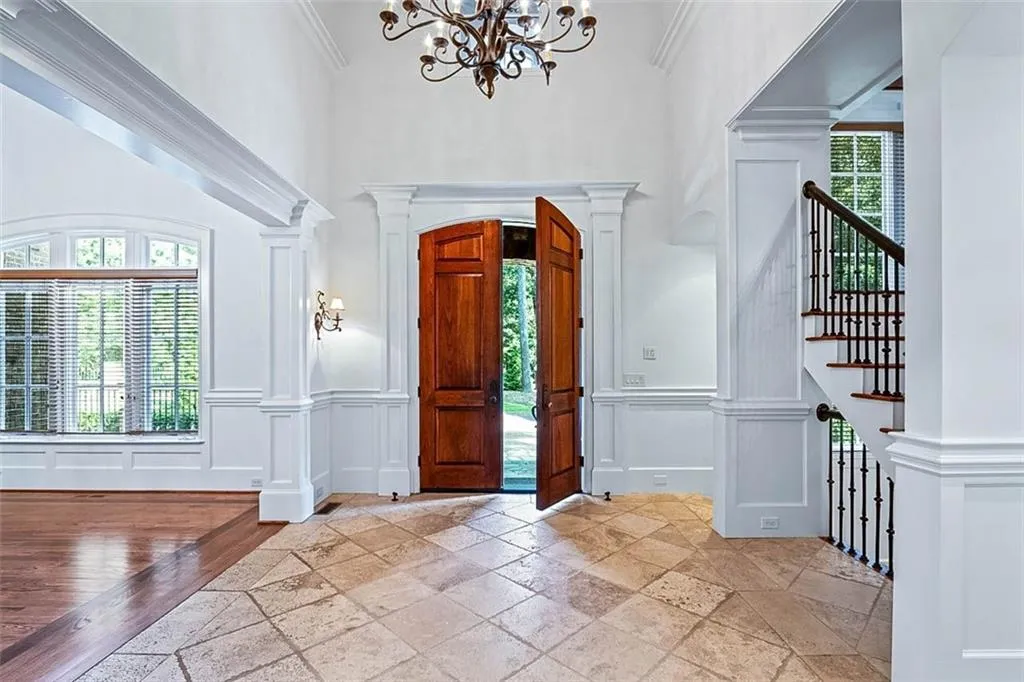 Foyer entrance featuring crown molding, an inviting chandelier, light tile flooring, and decorative columns