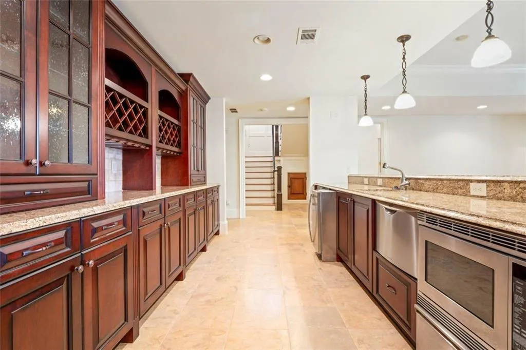 basement Kitchen with hanging light fixtures, light stone countertops, sink, and light tile flooring