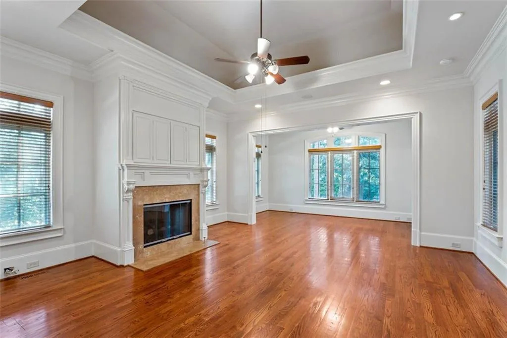 Unfurnished living room featuring a raised ceiling, ceiling fan, light hardwood / wood-style flooring, and plenty of natural light