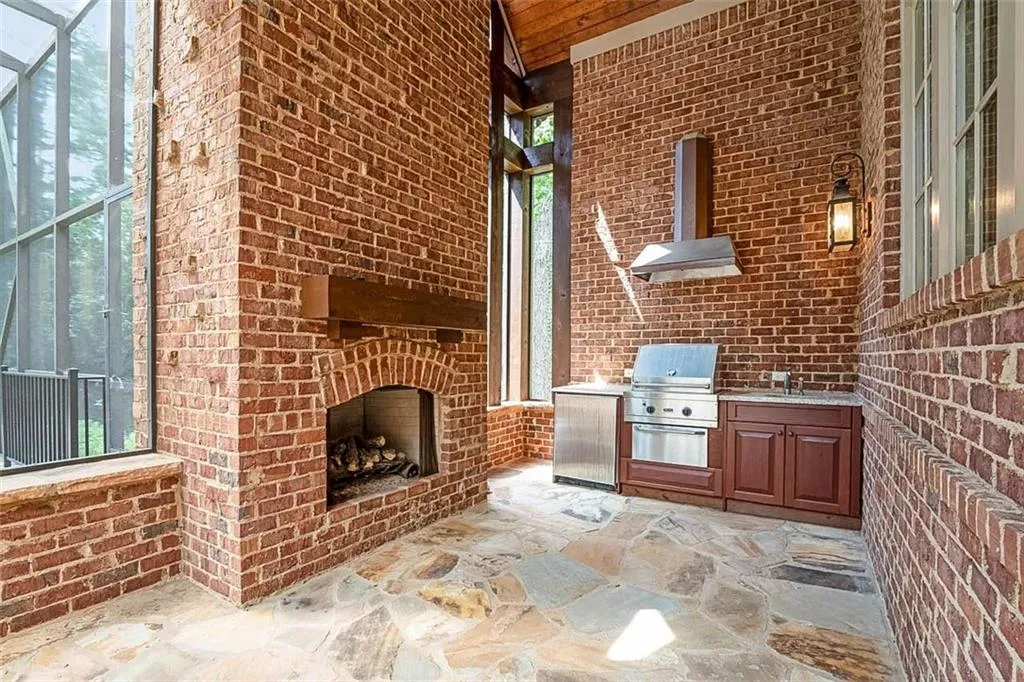View of patio / terrace with exterior kitchen, glass enclosure, a grill, sink, and a brick fireplace