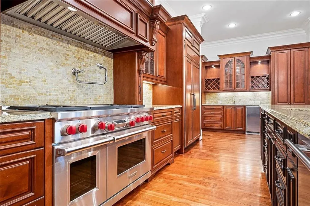 Kitchen with light wood-type flooring, high quality appliances, light stone countertops, tasteful backsplash, and premium range hood
