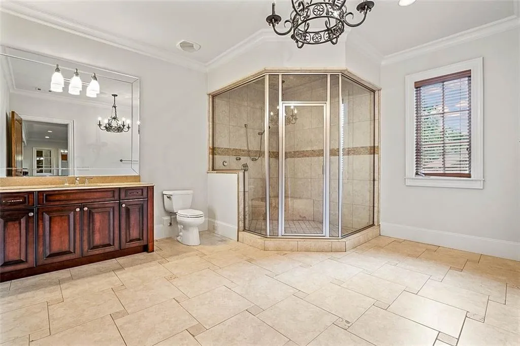 basement Bathroom featuring vanity, walk in shower, a notable chandelier, ornamental molding, and toilet