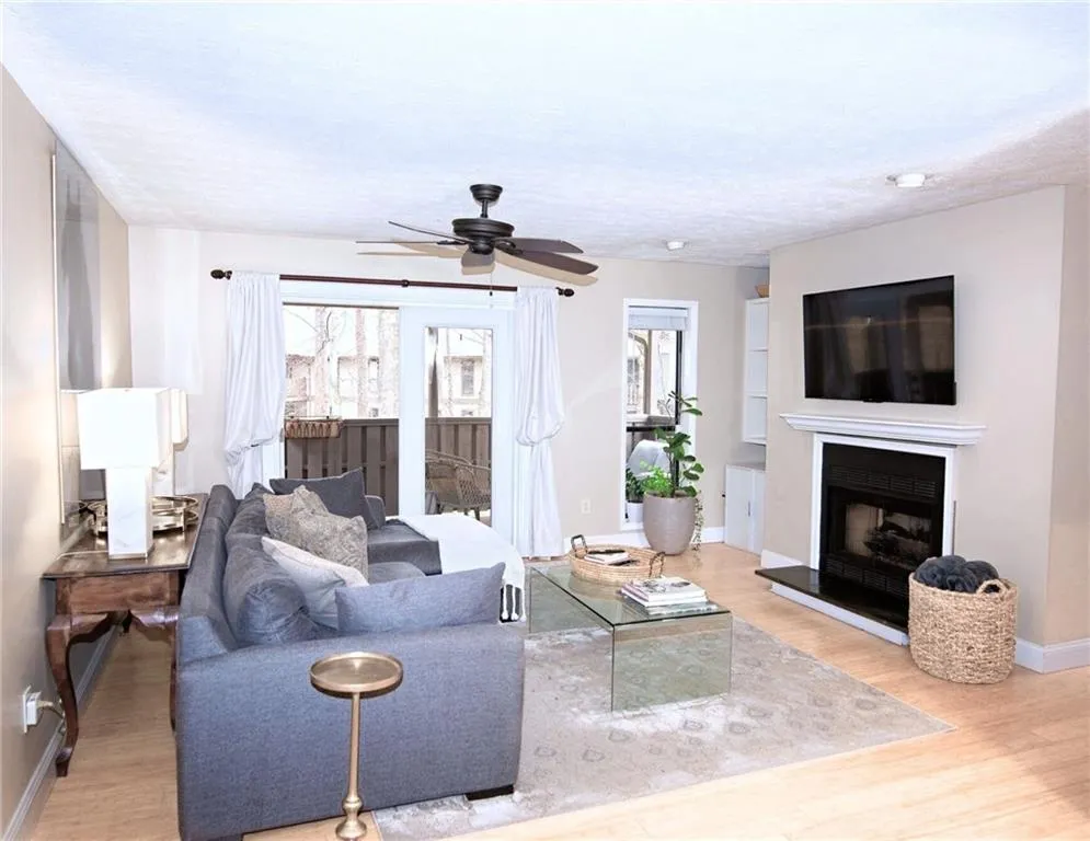 Living area with light wood-style flooring, ceiling fan, and a fireplace with raised hearth