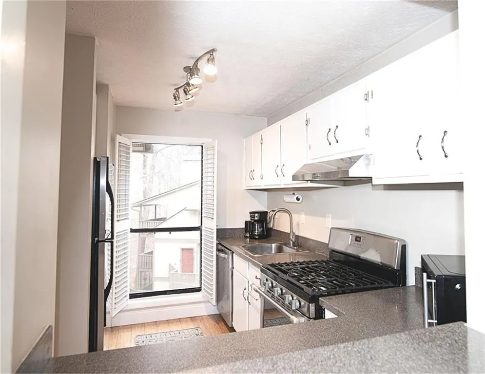 Kitchen featuring stainless steel appliances, white cabinets, light wood finished floors, a textured ceiling, and dark countertops