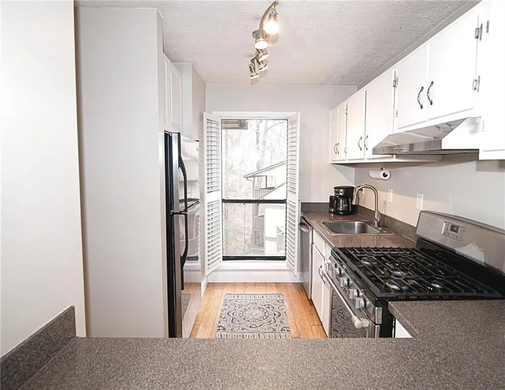 Kitchen with stainless steel appliances, light wood finished floors, a textured ceiling, dark countertops, and white cabinets