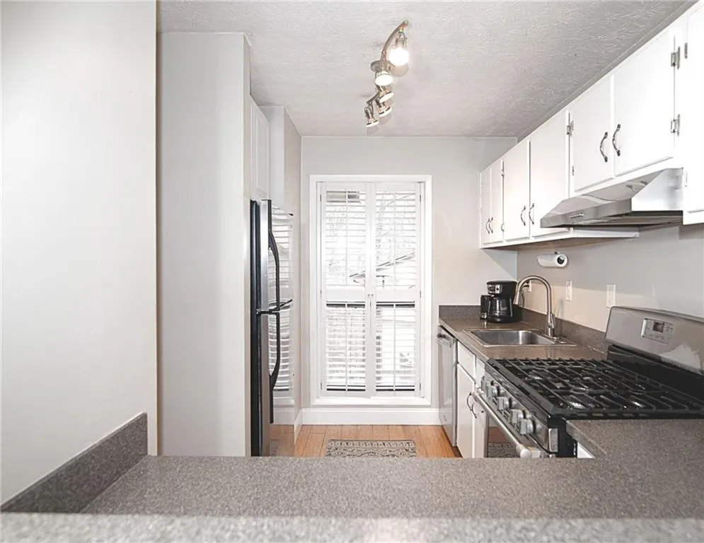 Kitchen featuring stainless steel appliances, light wood-style floors, white cabinets, rail lighting, and a textured ceiling