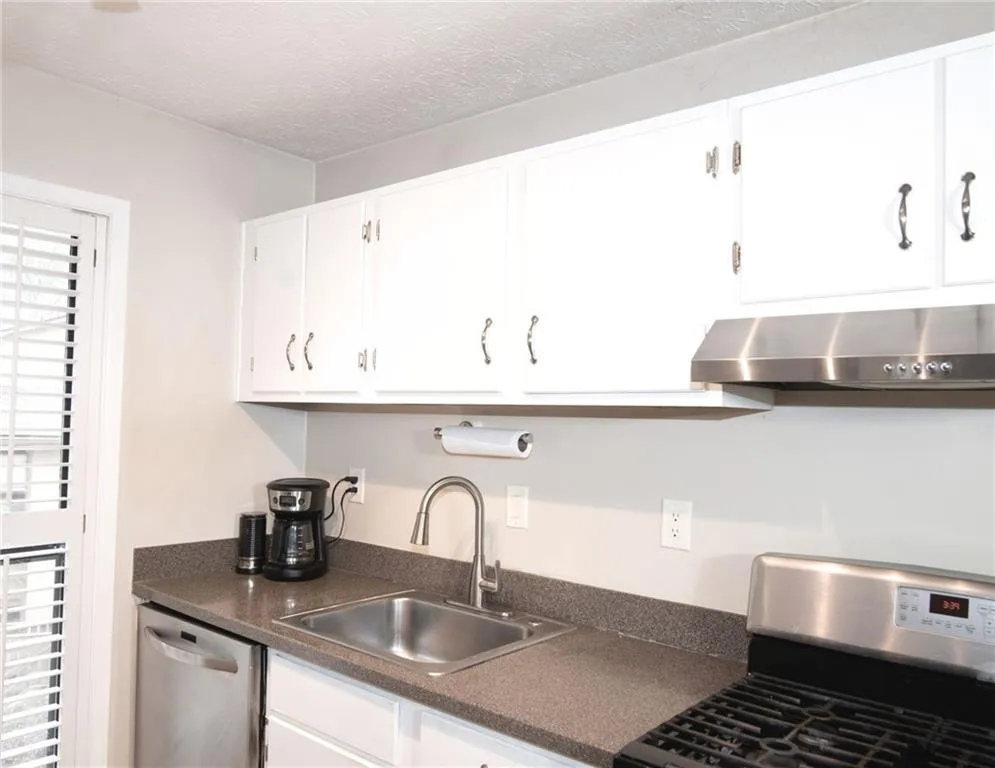 Kitchen with stainless steel appliances, dark countertops, and white cabinetry