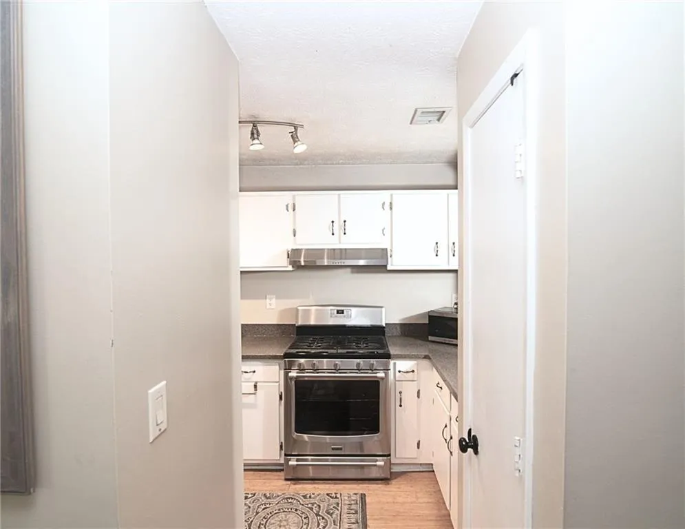 Kitchen with gas stove, white cabinets, light wood-type flooring, a textured ceiling, and track lighting