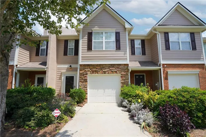 Exterior featuring stone facade detailing, vinyl siding, a two-car garage, and landscaped shrubbery