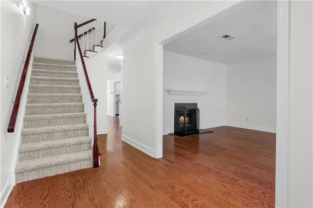 Stairs with crown molding, wood finished floors, and a warm lit fireplace
