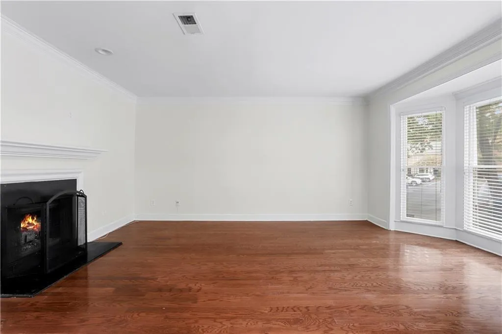 Unfurnished living room with dark wood-style floors, crown molding, and a lit fireplace