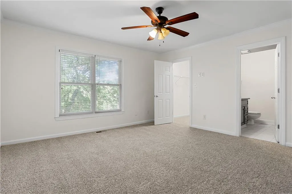 Unfurnished bedroom featuring ornamental molding, light carpet, a walk in closet, ceiling fan, and ensuite bathroom