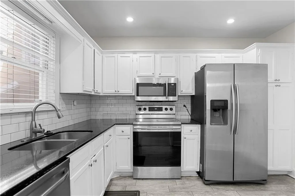 Kitchen with stainless steel appliances, tasteful backsplash, dark stone counters, white cabinetry, and recessed lighting