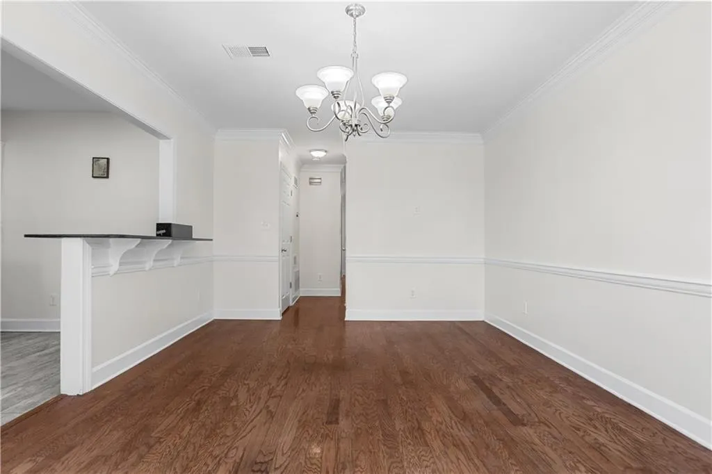 Unfurnished dining area featuring dark wood-type flooring, crown molding, and a chandelier