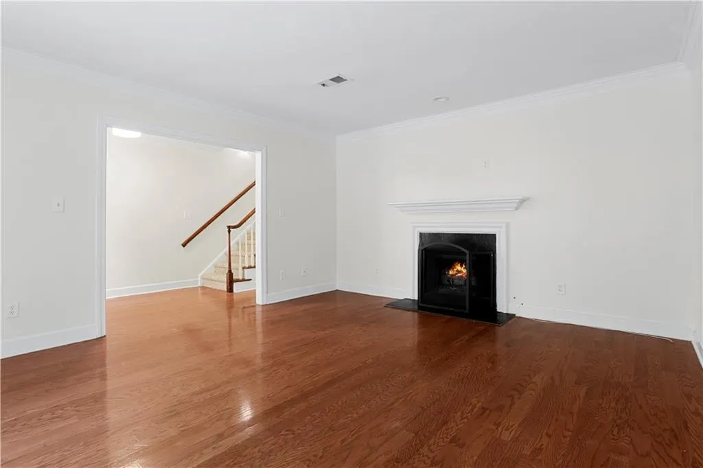 Unfurnished living room featuring ornamental molding, stairs, a warm lit fireplace, and dark wood finished floors