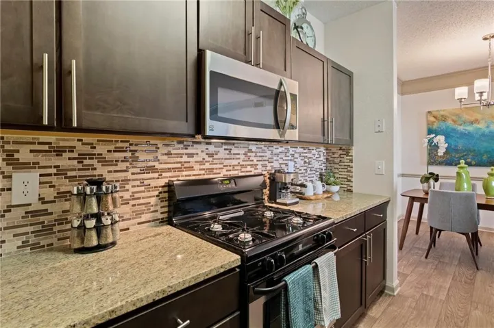 Kitchen with a textured ceiling, dark brown cabinets, stainless steel microwave, range with gas stovetop, and light wood finished floors