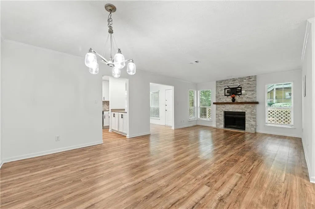 Unfurnished living room featuring light wood-style floors, a stone fireplace, ornamental molding, and a chandelier
