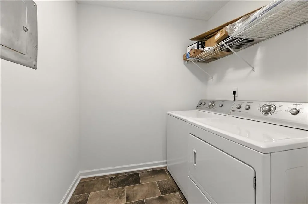 Laundry area with washer and dryer, electric panel, and stone finish flooring