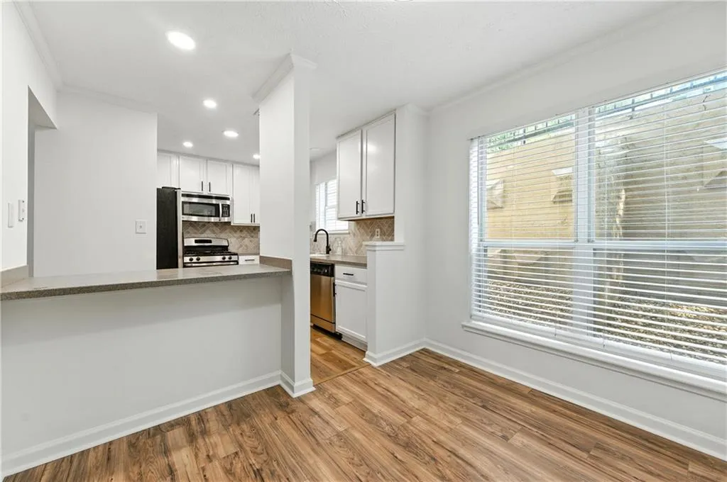 Kitchen featuring ornamental molding, wood finished floors, white cabinetry, stainless steel appliances, and tasteful backsplash