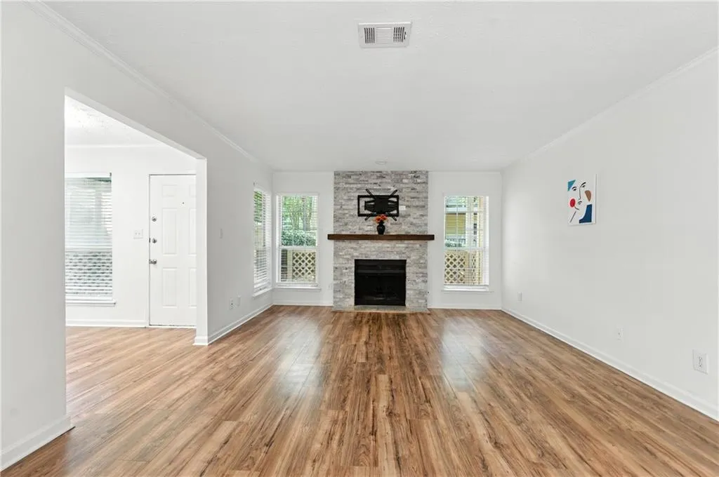 Unfurnished living room featuring ornamental molding, a stone fireplace, and wood finished floors