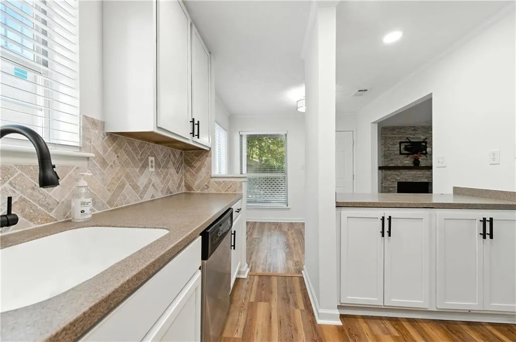 Kitchen with light wood-style floors, white cabinetry, dishwasher, crown molding, and backsplash