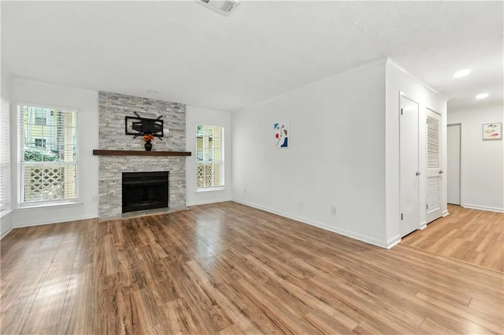 Unfurnished living room with ornamental molding, light wood finished floors, a stone fireplace, and a textured ceiling