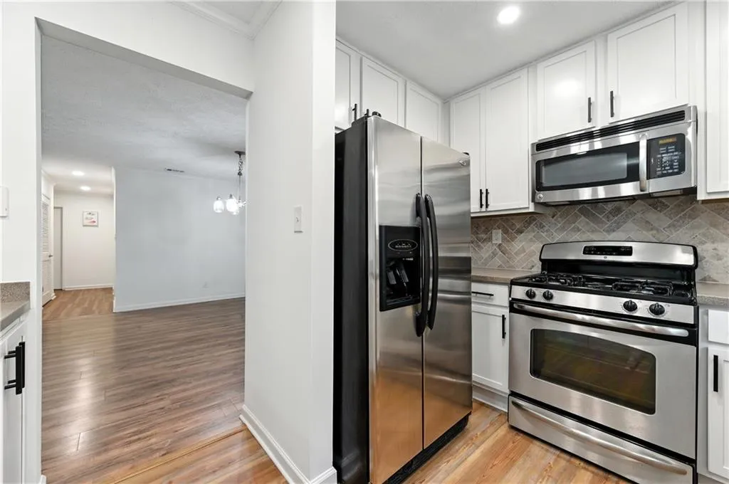 Kitchen with appliances with stainless steel finishes, light wood finished floors, decorative backsplash, white cabinets, and recessed lighting
