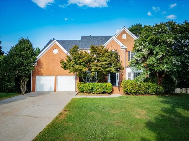 Brick exterior with a gabled roofline, featuring a two-car garage, established front landscaping, an inviting front entry, and multiple windows with shutters