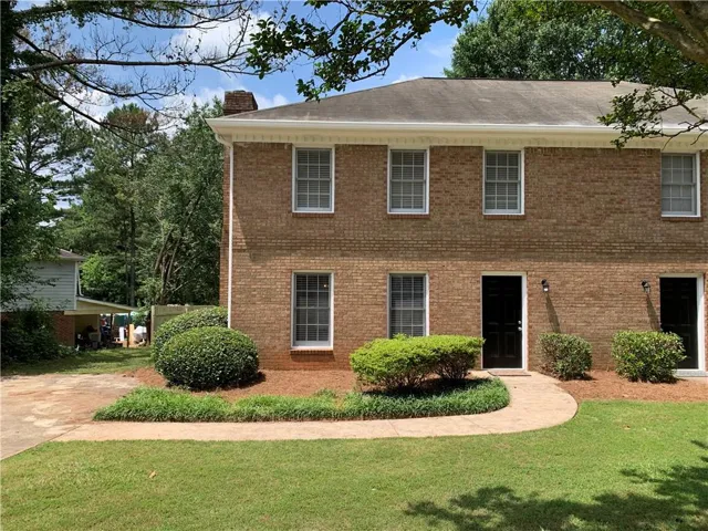Brick exterior residence with a curved concrete walkway, mature shrubbery, and a manicured lawn