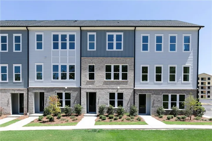 Modern townhome exterior featuring a combination of brick and siding, multiple large windows across three levels, a dark shingle roof, and landscaped entryways