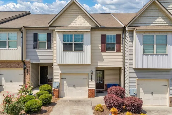 Two-story townhome featuring a neutral siding exterior, attached garage, and landscaped front entry