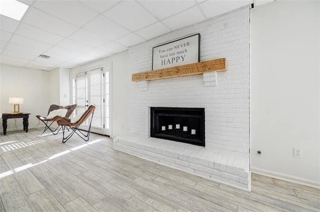 Unfurnished living room featuring a paneled ceiling, a brick fireplace, baseboards, and wood finished floors