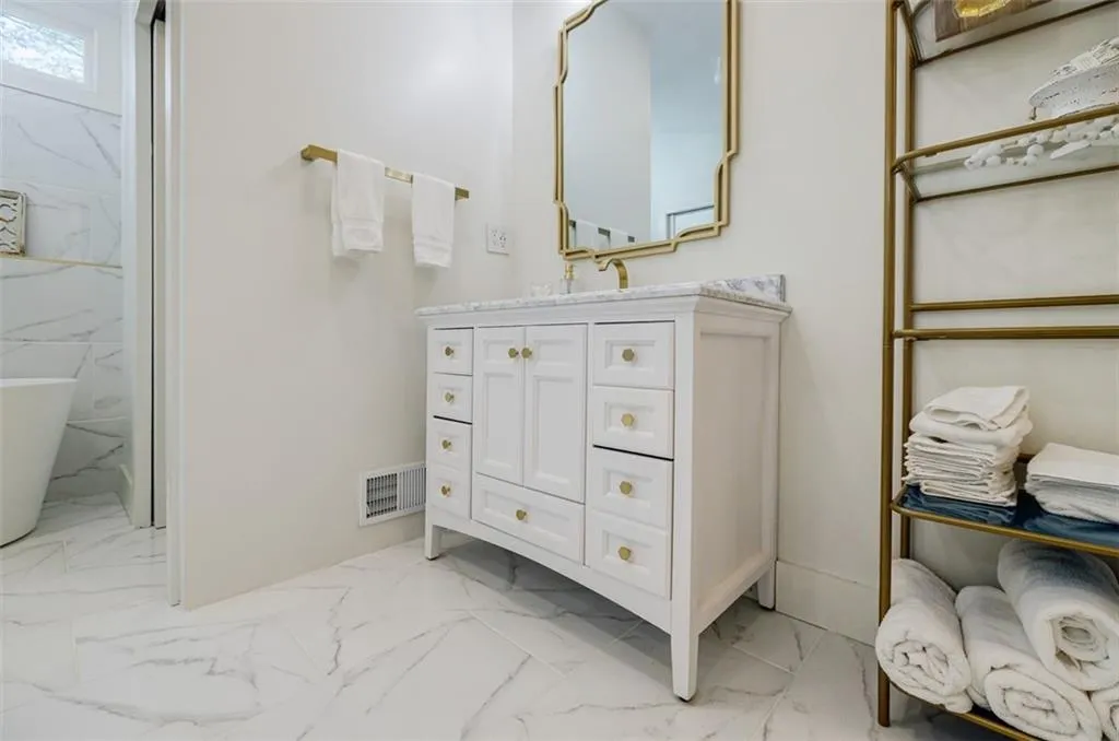 Bathroom with marble finish floor, vanity, a freestanding bath, and visible vents