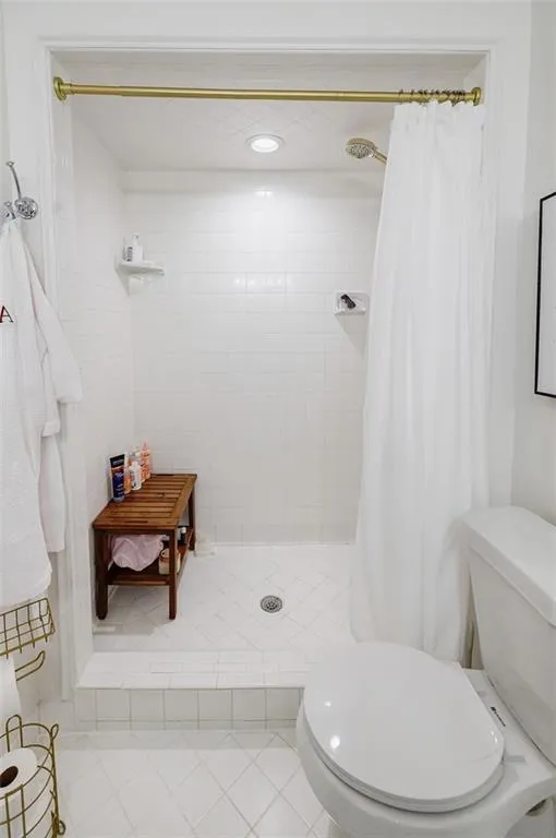 Bathroom featuring toilet, tile patterned flooring, and a tile shower