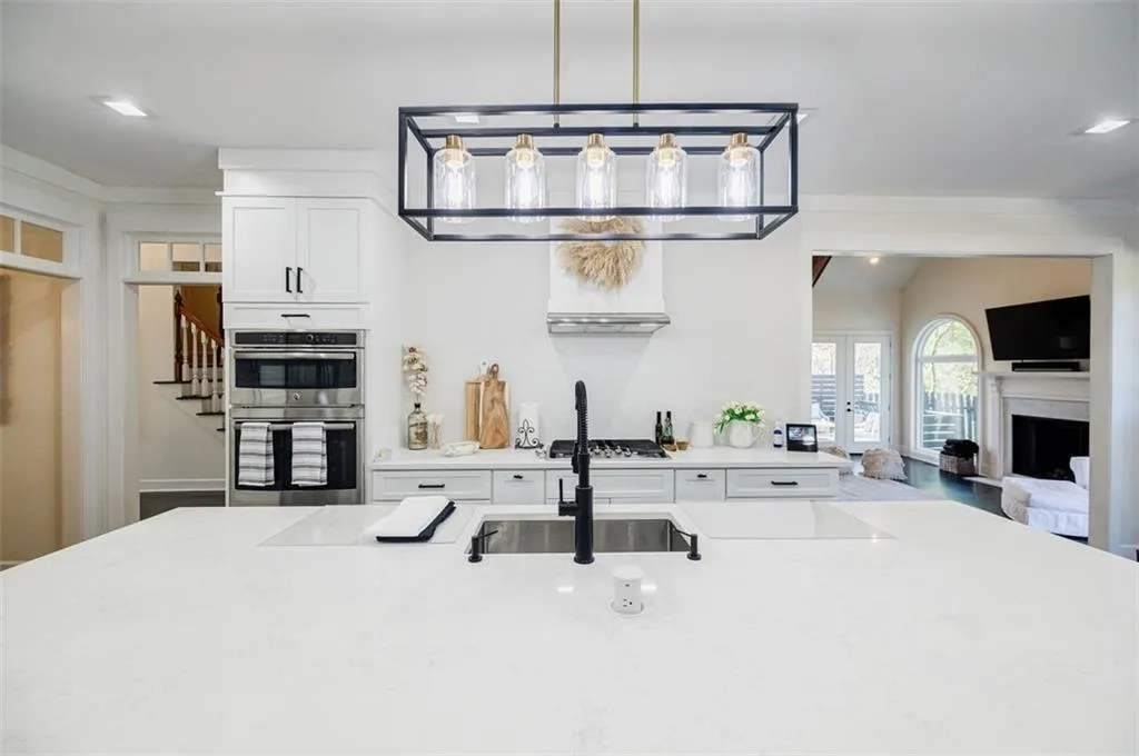 Kitchen featuring a sink, white cabinetry, a fireplace, stainless steel appliances, and decorative light fixtures