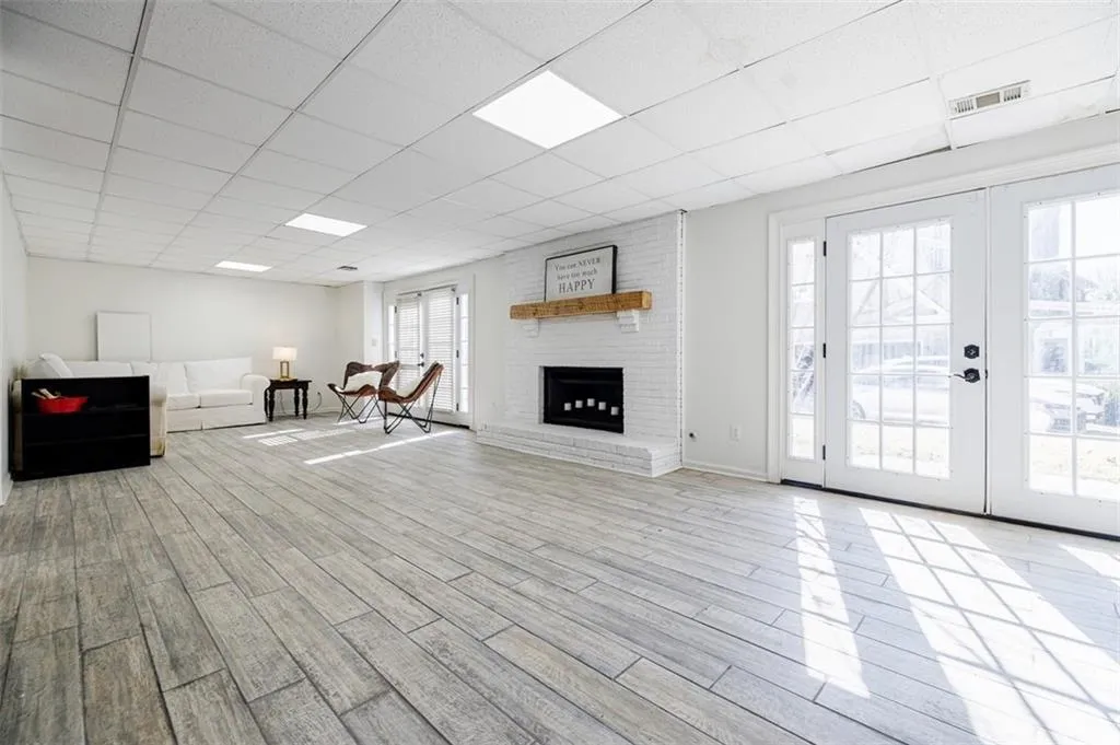 Unfurnished living room with french doors, wood finished floors, a brick fireplace, visible vents, and a paneled ceiling