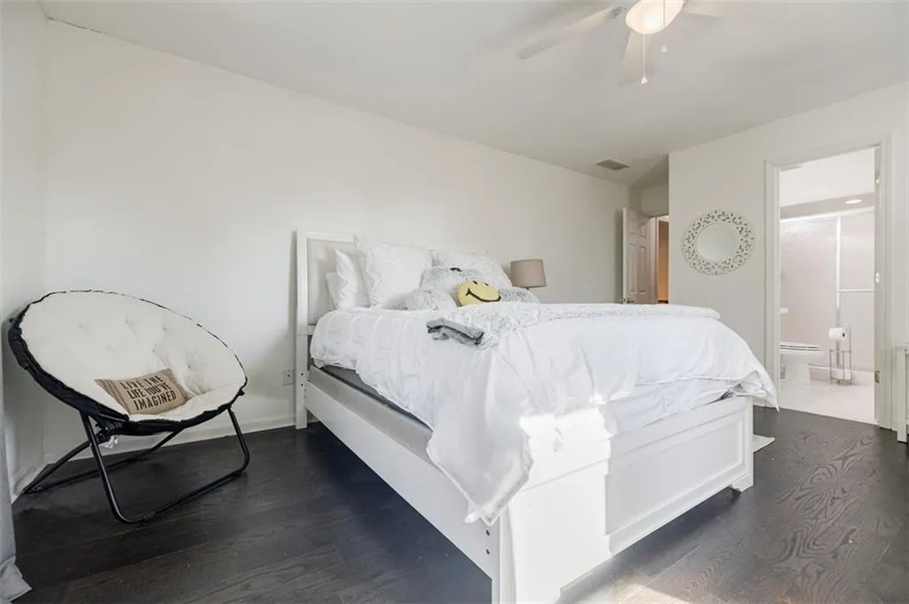 Bedroom with dark wood-type flooring, ensuite bath, ceiling fan, and visible vents