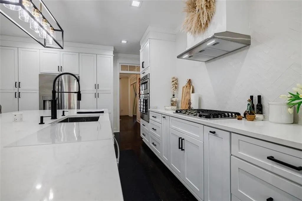 Kitchen featuring white cabinets, stainless steel appliances, tasteful backsplash, a sink, and wall chimney range hood